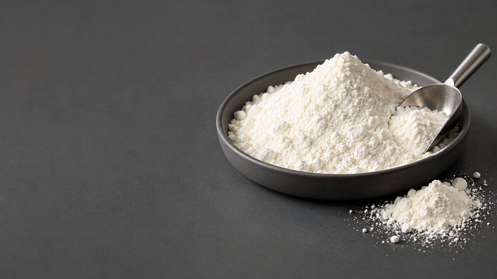 Fine white ingredient powder in a graphite dish with a stainless steel scoop